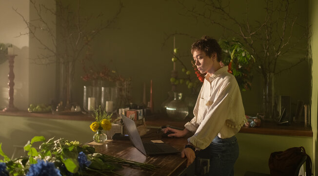 Female entrepreneur works on laptop at counter in flower shop.