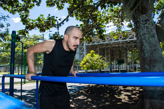 Man Performs Exercises on Bars in Park During Sunny Day