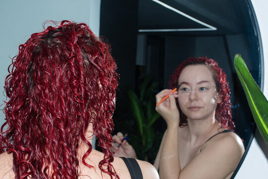 Woman Applying Makeup in Front of a Mirror at Home