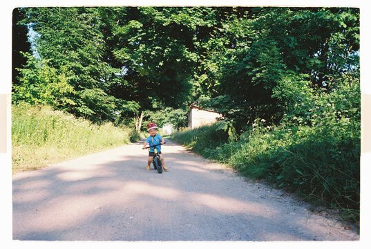 Little boy riding a balance bike down a shaded country lane