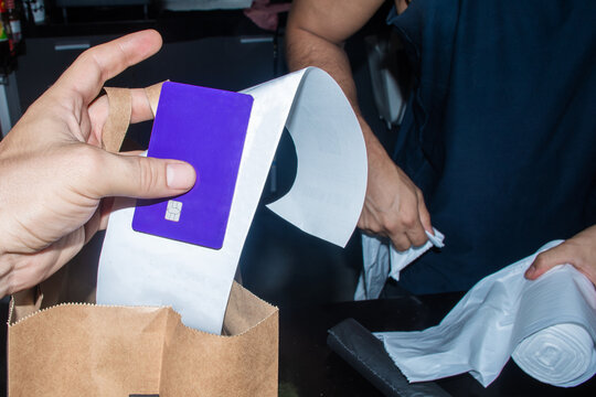 Person Holding a crdit Card While Another Person Prepares a Bag