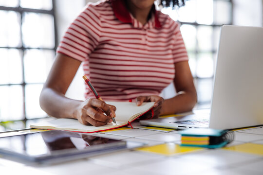 Woman Writing Notes While Working on a Laptop at a Desk