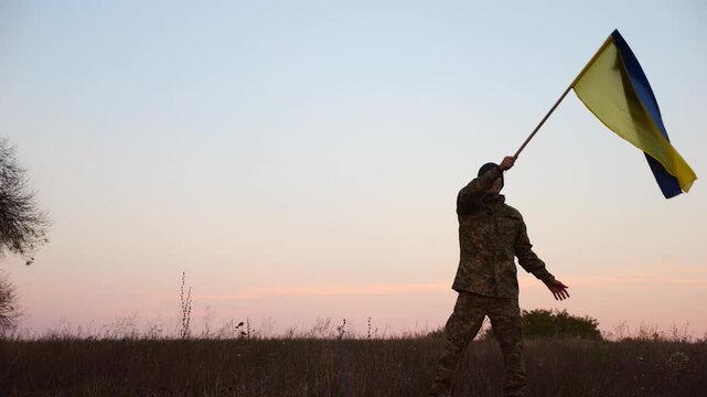 Male military waving blue-yellow banner on liberated territory occupied by russia. Young soldier of ukrainian army lifted flag of Ukraine in honor of victory against russian aggression at dusk