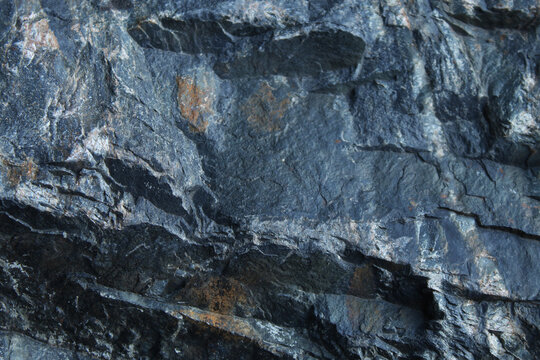 Rugged dark grey rock face with sharp faceted texture and deep crevices