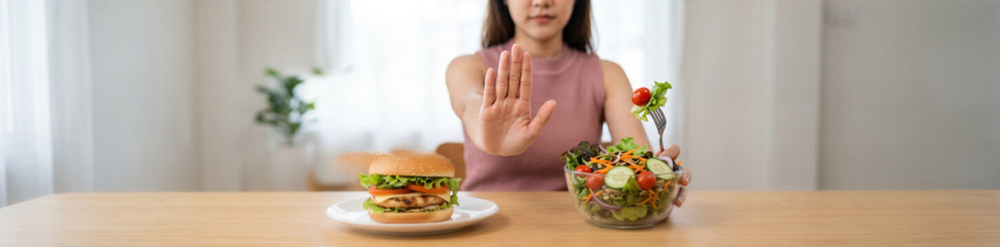 Person choosing a fresh vegetable salad instead of a high-calorie burger, showing a stop gesture toward junk food while following a healthier diet for weight control, healthy diet, fast food refusal, 