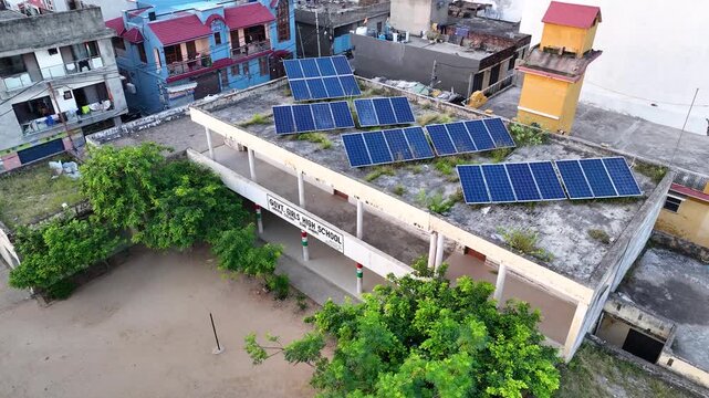 Drone orbit shot around a government school building equipped with rooftop solar panels in India, showcasing clean green energy infrastructure.