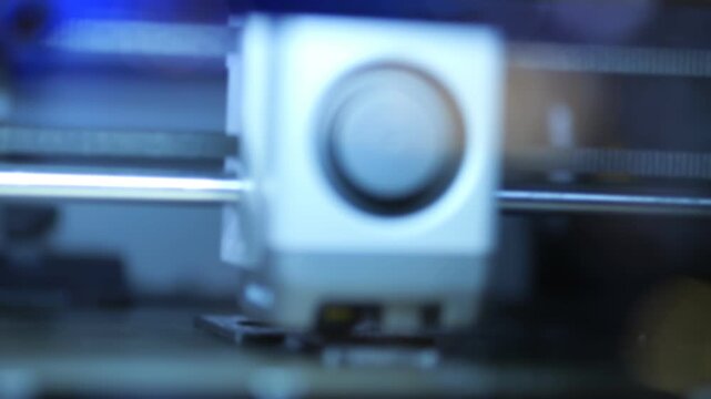 Three keyframes show a 3D printer in operation. Printer head moves slowly with precision. Blue light illuminates the mechanical parts. Focus shifts slightly between frames