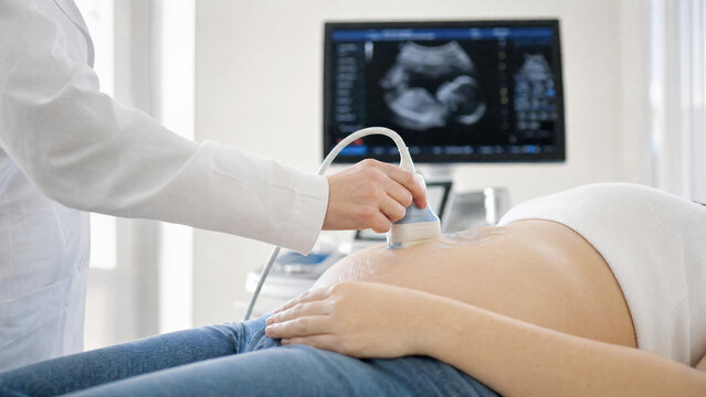 Close-up of pregnant woman receiving prenatal ultrasound scan from healthcare professional in modern medical clinic, with fetal sonogram displayed on monitor during routine maternity examination and p