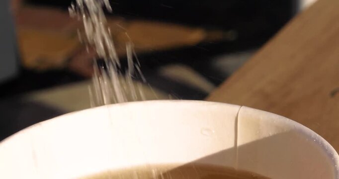 Close-up shot of pouring sugar from a packet into tea