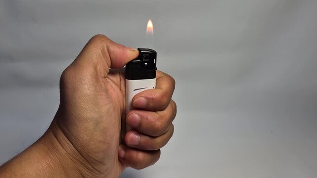 Close-up of a hand holding a white and black lighter, igniting a flame with a transparent background, stop motion sequence