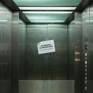 Industrial metal elevator interior with no smoking sign, stainless steel lift cabin with control panel, empty commercial building elevator
