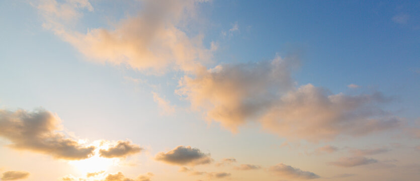 Panoramic Golden Hour Sky with Soft Clouds at Sunset,A wide panoramic photograph of a soft sunset sky featuring golden-lit clouds against a blue and pale yellow gradient backdrop. Ideal for web header