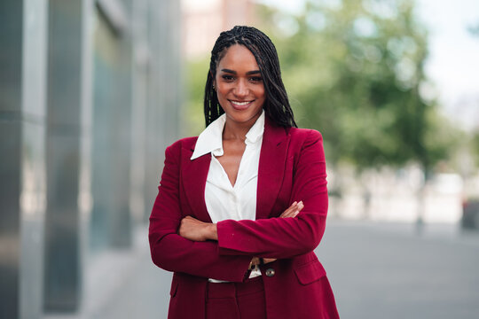 Confident black businesswoman standing with folded arms, smiling outdoors, representing leadership and success in a corporate setting