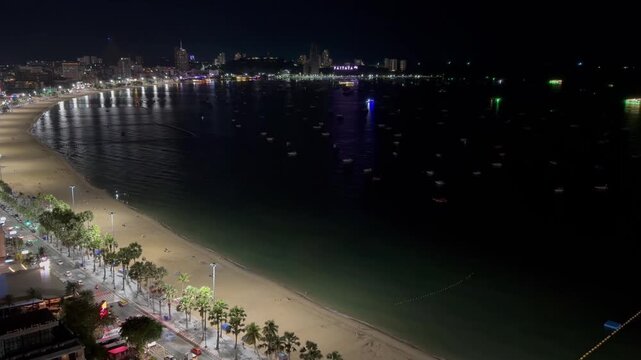 Night aerial view of Pattaya Beach and coastline in Chon Buri, Thailand, illuminated by vibrant city lights, street traffic, and anchored boats.