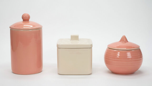 Three ceramic kitchen canisters with lids in soft pink and cream colors on white background