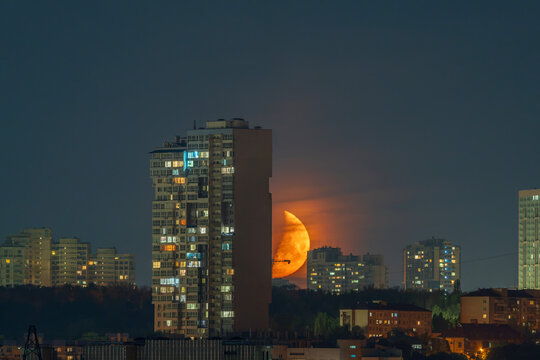Beautiful wide view of a giant orange moon rising behind a high rise city building at night