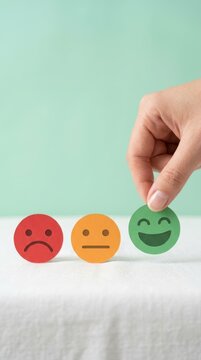 A hand selecting a happy green smiley face icon among sad and neutral emotion icons for customer feedback