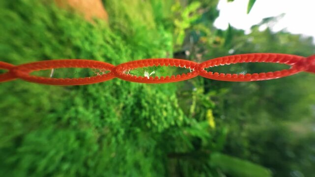 Bright orange plastic chain links hanging outdoors against blurred green foliage