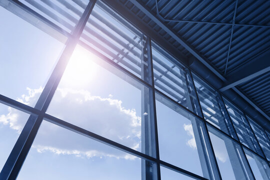 Modern glass facade and sunlight background. Steel window framework under blue sky. Commercial building interior. Sun rays through large windows. Architectural structure and bright daylight.
