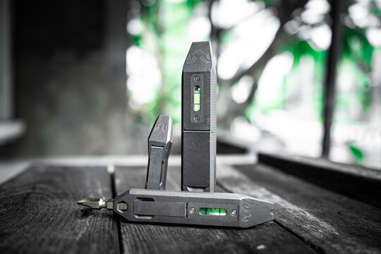 Titanium EDC pry bar multi tools with green tritium vials on dark wooden table outdoors