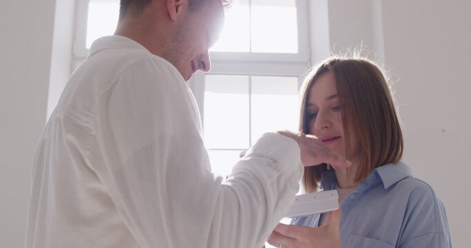 Couple giving gift box, tender surprise moment. Man offers a small red present and the woman smiles. Anniversary romance, celebration, romantic relationship and Valentines day concept. 