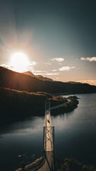 Aerial vertical view of a suspension bridge over a fjord with mountains and road during a bright sunset in Norway © Quality by Simon