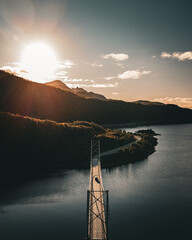 Aerial vertical view of a suspension bridge over a fjord with mountains and road during a bright sunset in Norway © Quality by Simon