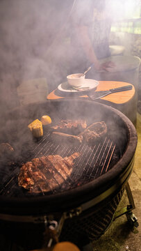 Gourmet meat cuts grilling on a barbecue pit with smoke rising in an atmospheric outdoor kitchen