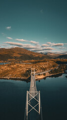 Vertical aerial view of a symmetrical suspension bridge crossing a fjord towards autumnal mountains in Norway with copy space © Quality by Simon