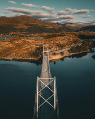 Vertical aerial view of a symmetrical suspension bridge crossing a fjord towards autumnal mountains in Norway with copy space © Quality by Simon