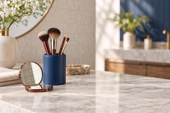 Makeup brushes in blue holder and open compact mirror on marble bathroom counter. Morning beauty routine concept with natural sunlight. Copy space