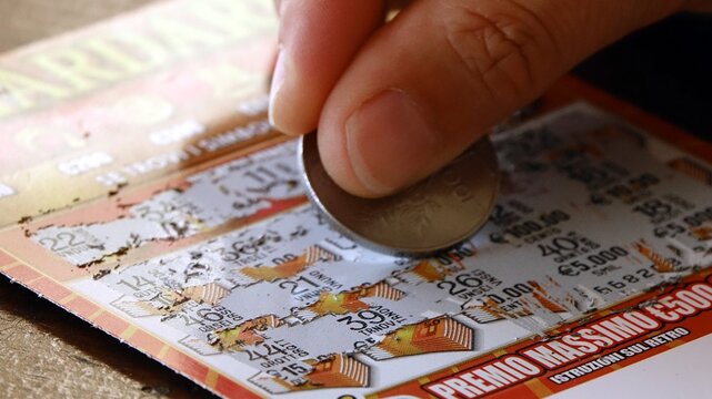 Milano, Italy - 09.19.2026: scratching a scratch-off ticket concept: Close up of a person using a coin to scratch off a lottery ticket for a chance at a prize. 