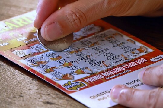 Milano, Italy - 09.19.2026: scratching a scratch-off ticket concept: Close up of a person using a coin to scratch off a lottery ticket for a chance at a prize. 