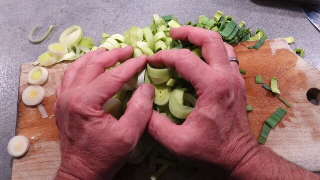 Stockholm, Sweden A cook's hands grab a handful of sliced leeks on a wooden board. 