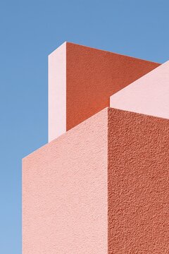 Minimal geometric architecture with coral pink textured walls against a clear blue sky
