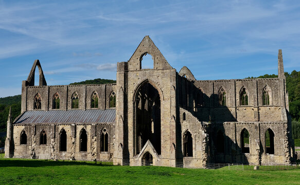 Historic Tintern Abbey, a medieval Gothic monastery in the Wye Valley, Wales, United Kingdom, photographed on a sunny day with blue sky and green countryside.