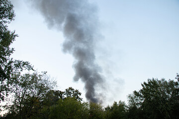 Obraz premium Thick black smoke rises above the trees after a drone attack in Ukraine. The concept of fire, missile attack, drone raid