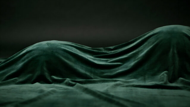 Human body silhouette covered with dark green velvet fabric, abstract artistic composition with soft folds and shadows on a dark background