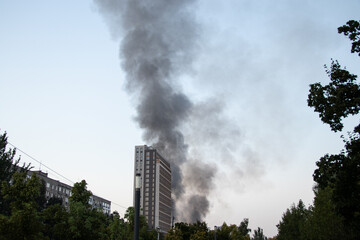 Obraz premium Thick black smoke rises from the top of an apartment building after a drone attack in Ukraine. The concept of fire, missile attack, drone raid