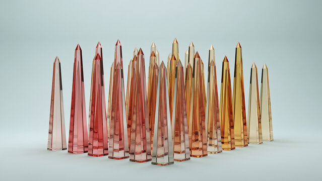 Numerous translucent glass obelisks in gradient colors of pink, peach, and amber arranged in a group on a light blue studio background