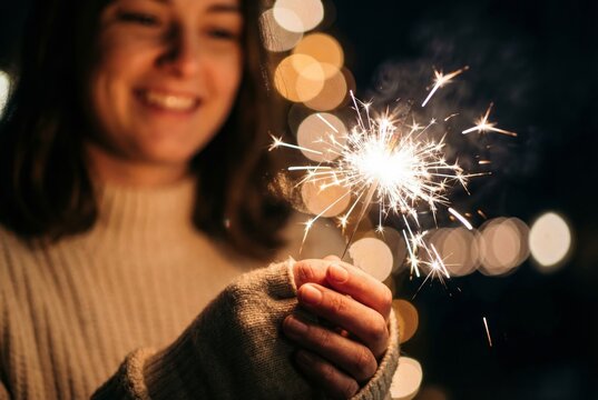 Young woman holding burning sparkler at night with Christmas lights bokeh background