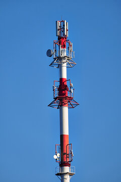 Red and white telecommunications tower with cellular antennas and communication equipment against a clear blue sky, isolated vertical composition with ample copy space