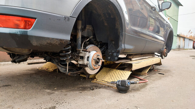 Car with the wheel removed, exposing the brake disc, suspension and wheel hub, with an impact wrench on the ground during automotive repair and maintenance