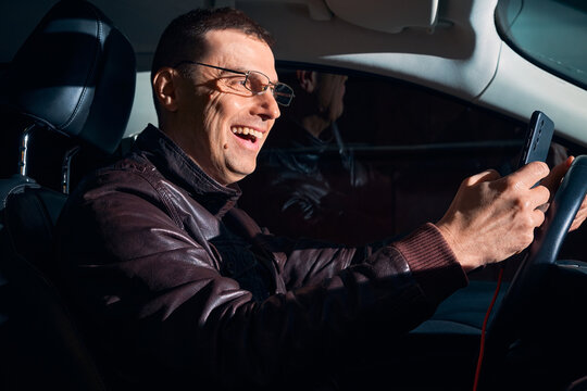 Excited middle aged man using smartphone while driving car at night