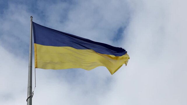 National blue and yellow flag of Ukraine waving in wind against cloudy sky on tall flagpole