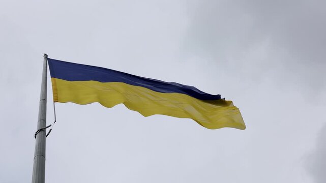 National blue and yellow flag of Ukraine waving in wind against cloudy sky on tall flagpole