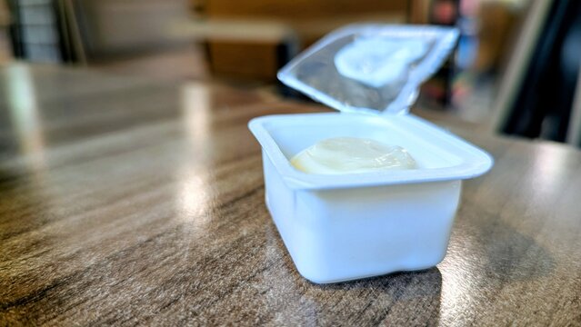 Single-use plastic container of Parmesan sauce alongside fast food. Highlights convenience but hints at excessive consumption and environmental concerns related to packaging waste.