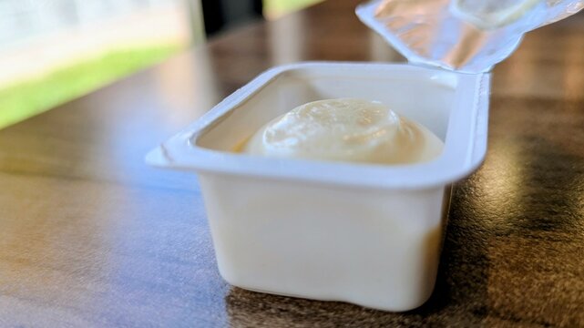 Single-use plastic container of Parmesan sauce alongside fast food. Highlights convenience but hints at excessive consumption and environmental concerns related to packaging waste