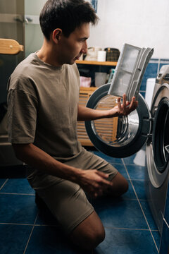 Vertical shot of focused man checking and cleaning tumble dryer lint filter, performing regular maintenance for efficient home appliance operation and longevity. Concept of household cleanliness.