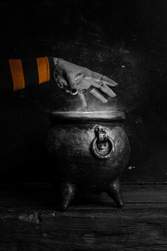 Witch's hand over a cauldron with a magic potion in a dark room. Witch casting spells on Halloween night